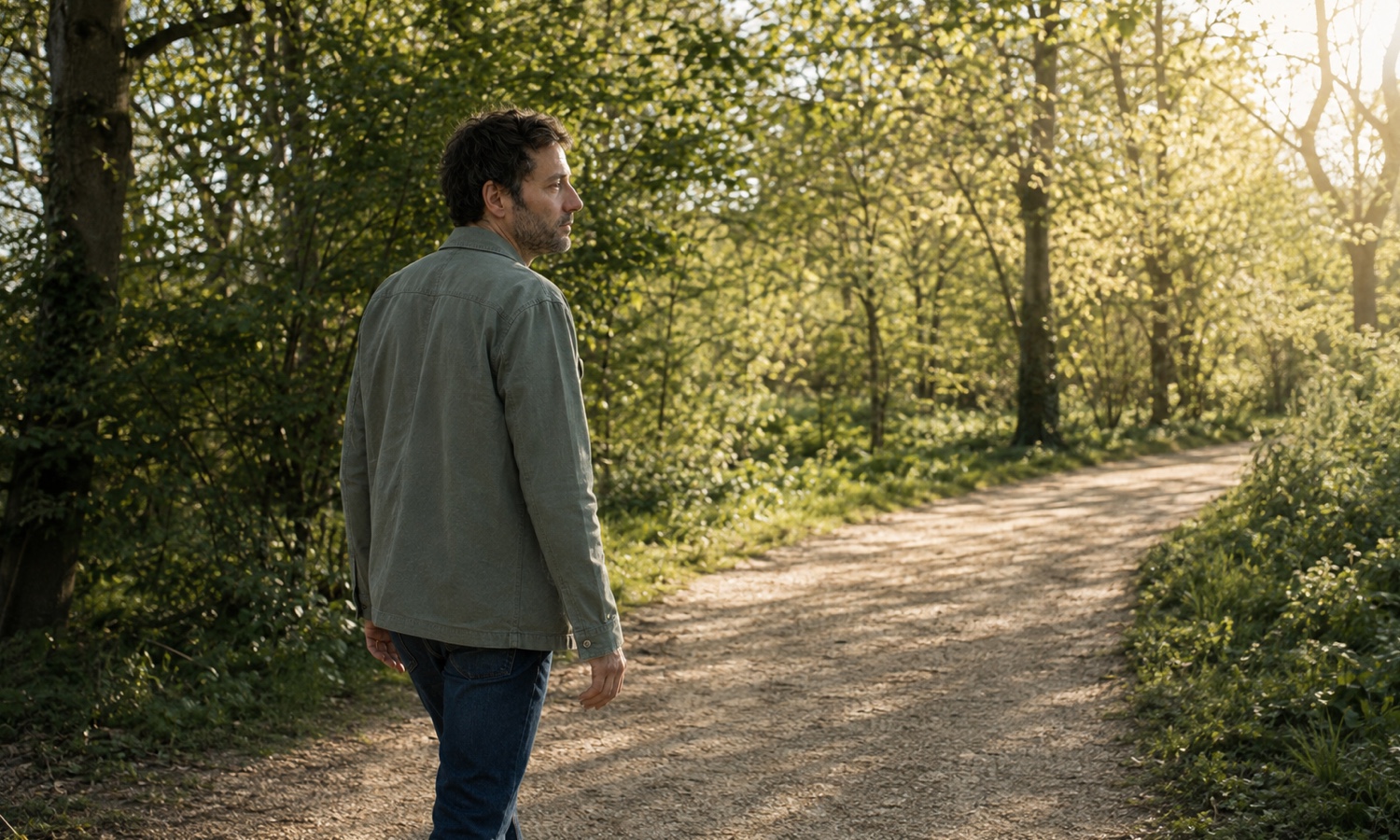 Une personne marche seule sur un chemin bordé d’arbres, dans une lumière douce de fin d’après-midi